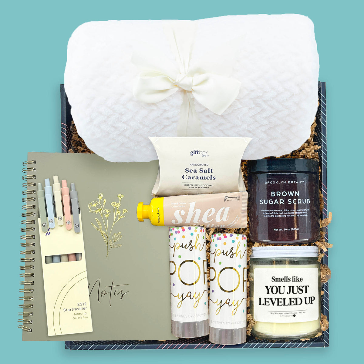 A Moment to Celebrate gift box with blanket, candle, spa items, notebook, and treats