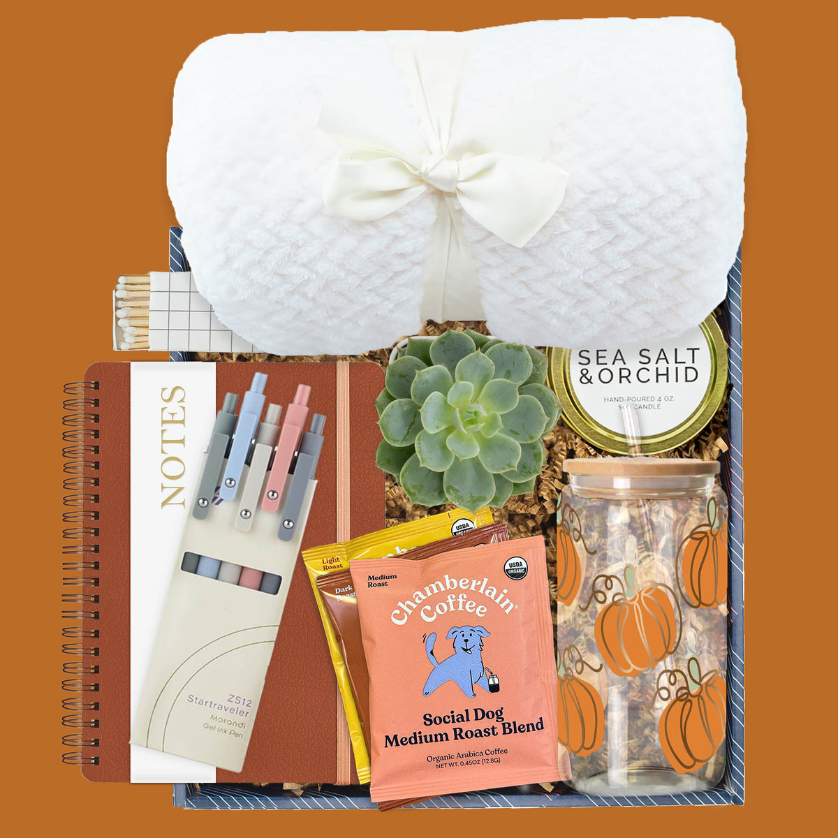 Autumn Brew Gift Box with plush blanket, pumpkin glass tumbler, notebook, gel pens, Chamberlain Coffee packets, succulent, soy candle, and decorative matches.