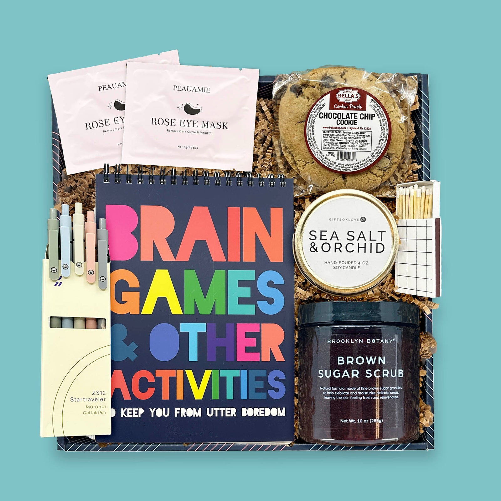 Brain games and spa treats gift box with candle, sugar scrub, eye masks, pens, and cookie