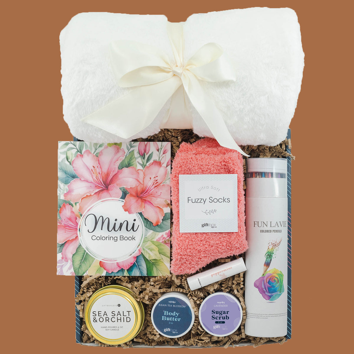 Creative & Cozy Self Care Gift Box with plush blanket, coloring book, colored pencils, fuzzy socks, candle, body butter, sugar scrub, and peppermint lip balm.