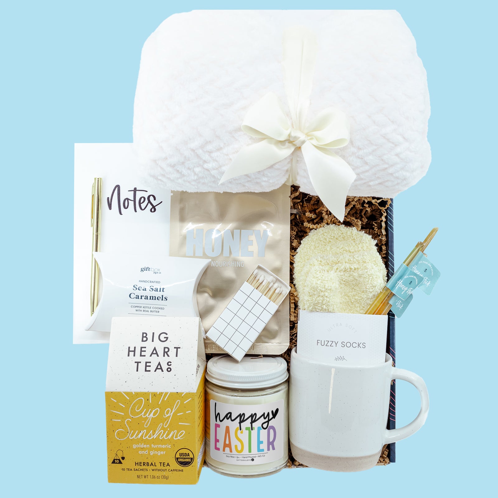 Easter Tea & Tranquility Gift Box featuring a cozy blanket, soy candle, mug, tea, fuzzy socks, caramels, face mask, journal, and handwritten card.