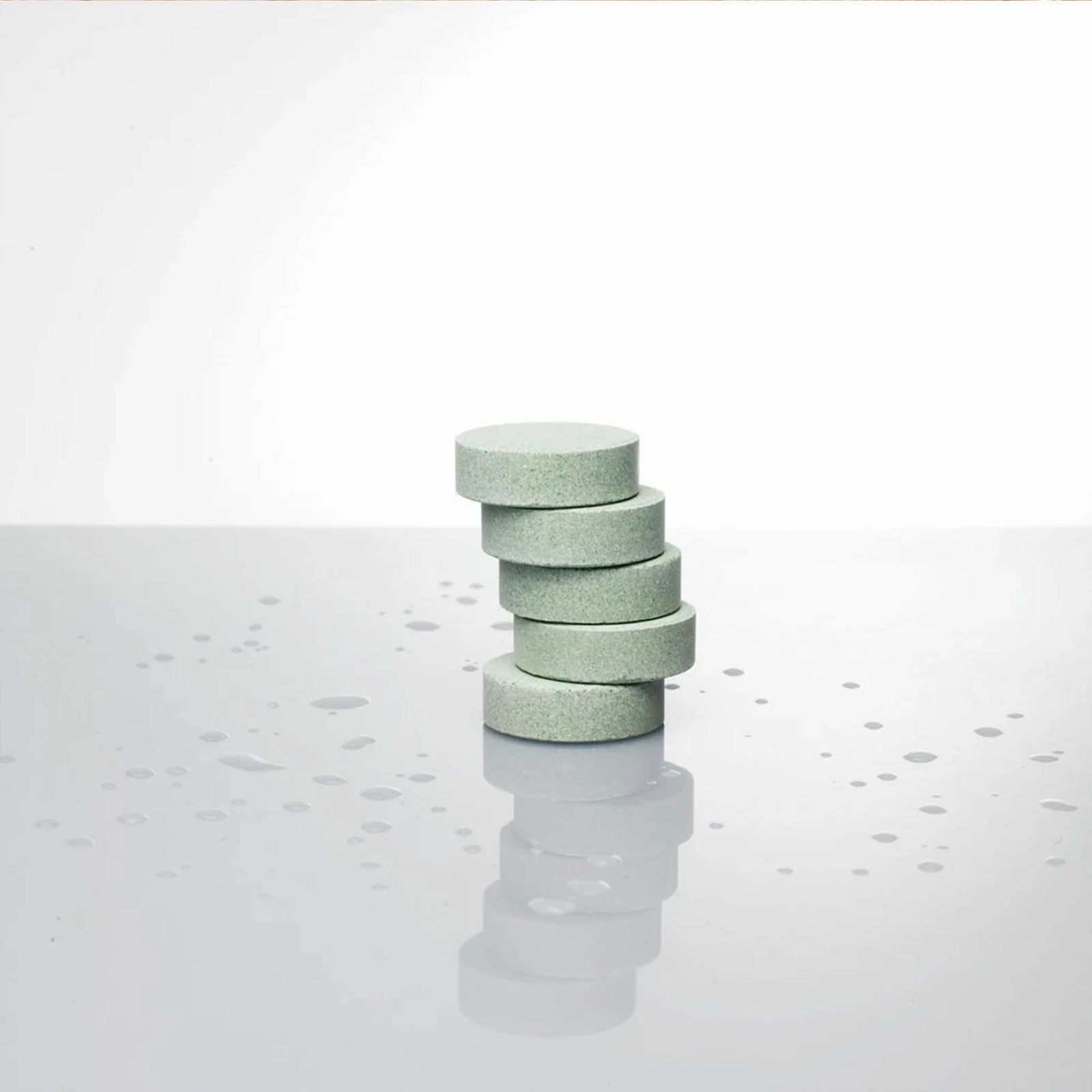Stack of eucalyptus shower steamer tablets on a reflective surface with water droplets