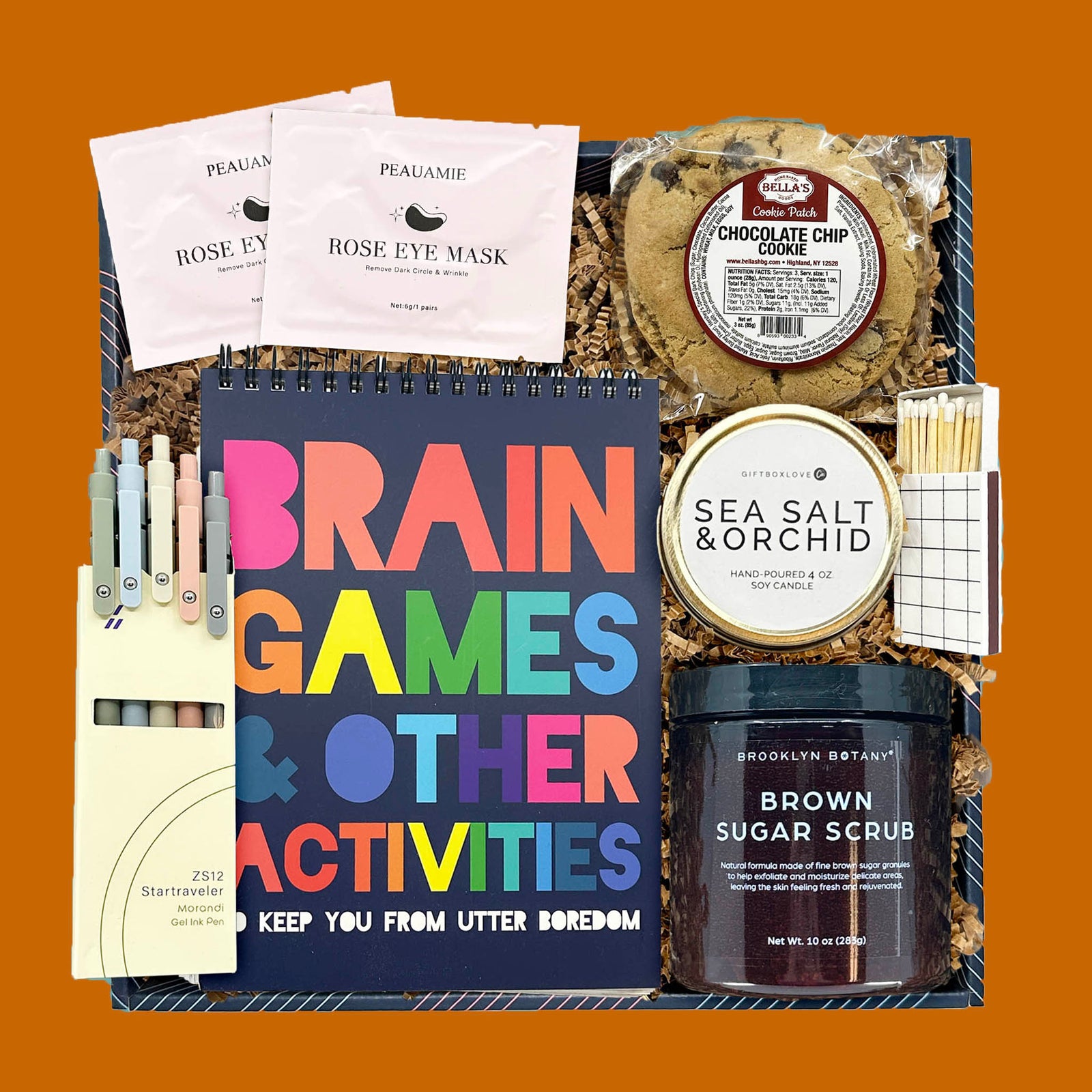 Fall Games & Retreat Gift Box with brain games book, gel pens, body scrub, candle, eye masks, chocolate chip cookie, and matches.