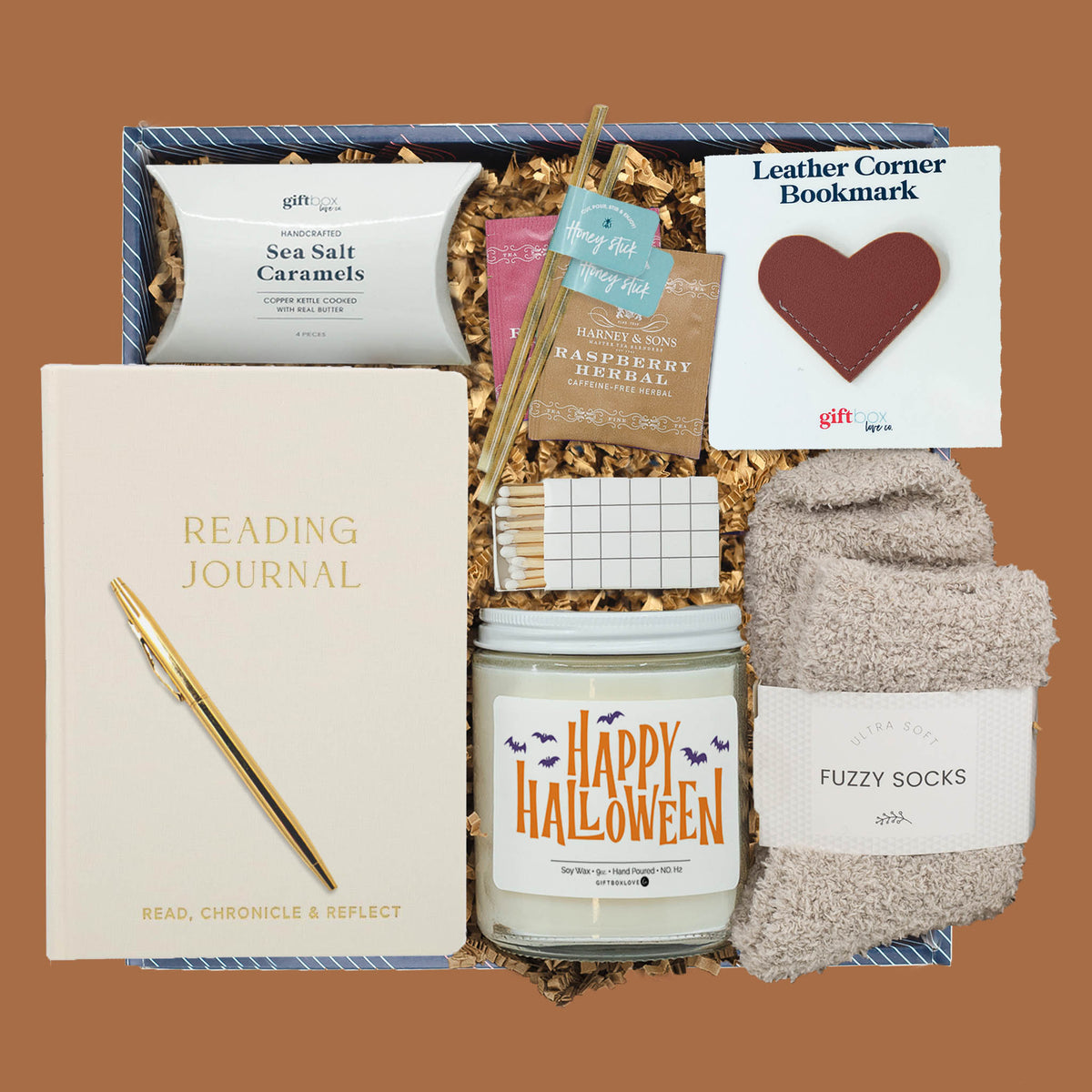 Ghostly Goodies Gift Box with reading journal, gold pen, leather bookmark, fuzzy socks, Halloween soy candle, herbal tea, honey sticks, sea salt caramels, and decorative matches.