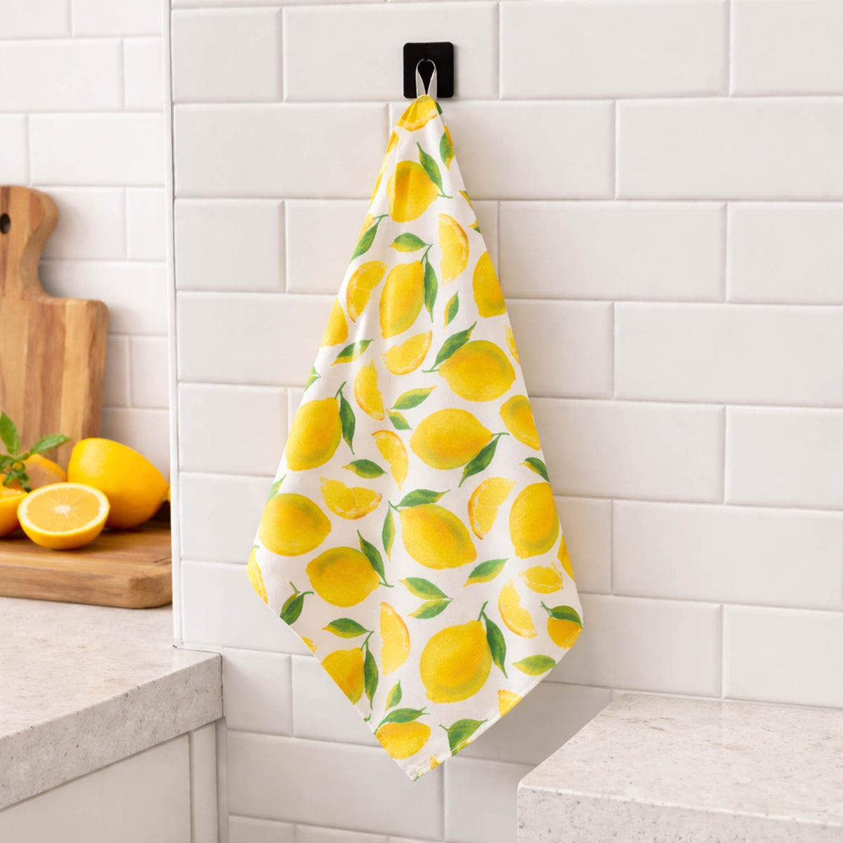 lemon print dish towel hanging in kitchen with yellow lemons and green leaves