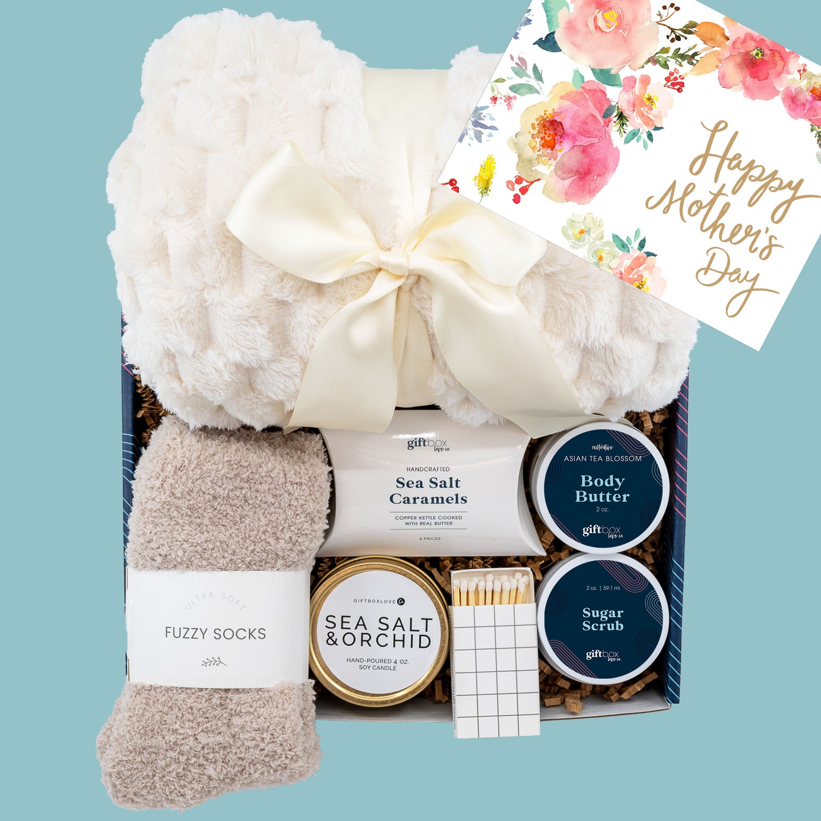 Mother’s Day gift box with cozy blanket, fuzzy socks, Sea Salt & Orchid candle, body butter, sugar scrub, caramels, and matches.