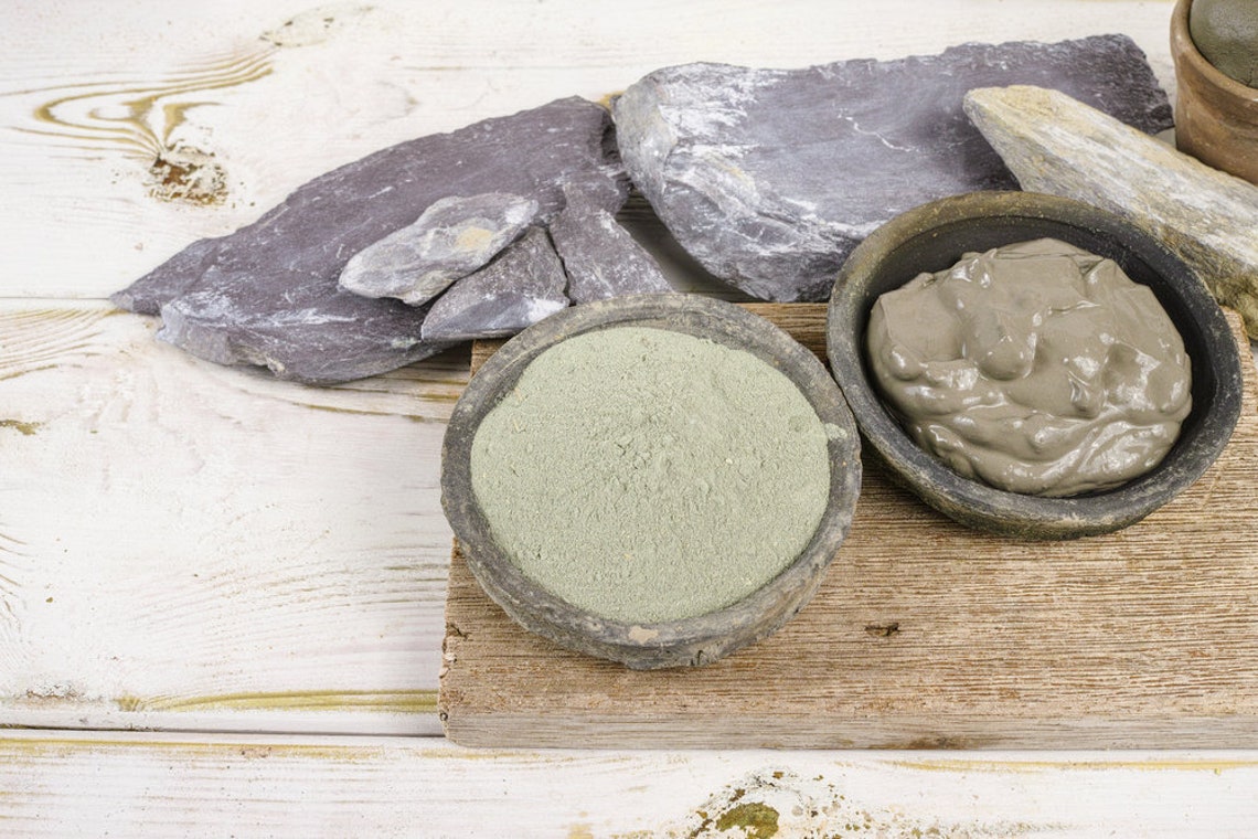 Natural French clay powder and creamy mask in stone bowls with slate rocks for spa skincare gift sets.